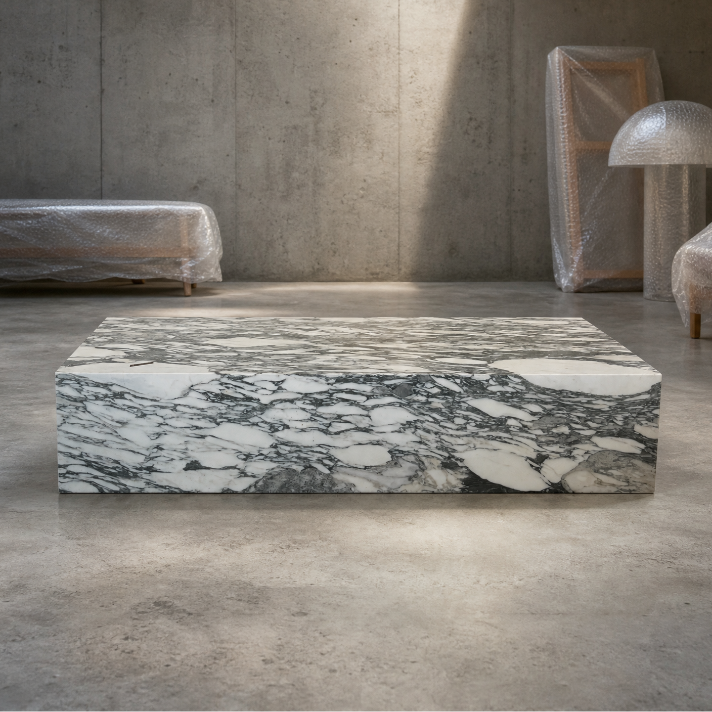 A rectangular coffee table made of calacatta verde marble sits in the center of a minimalist concrete room, surrounded by furniture wrapped in protective plastic.