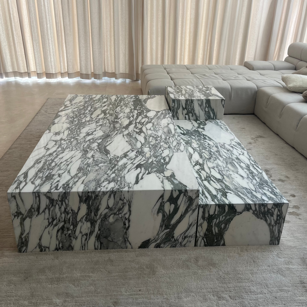 A modern rectangular coffee table made of white marble with dramatic green and gray veining, styled in a minimalist living room with a matching marble side table and a light gray sectional sofa in the background.