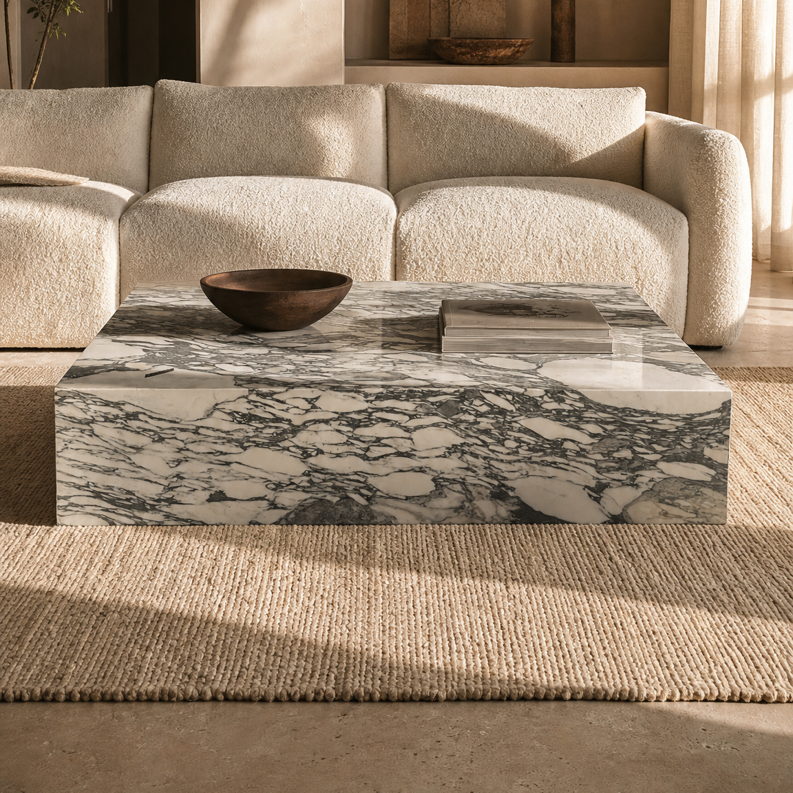 A modern living room scene featuring a low rectangular coffee table with a gray-green and white calacatta marble pattern, styled in front of a cream-colored textured sofa.