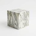 A cube-shaped side table or stool with a white marble pattern featuring gray and green veining, set against a plain white background.