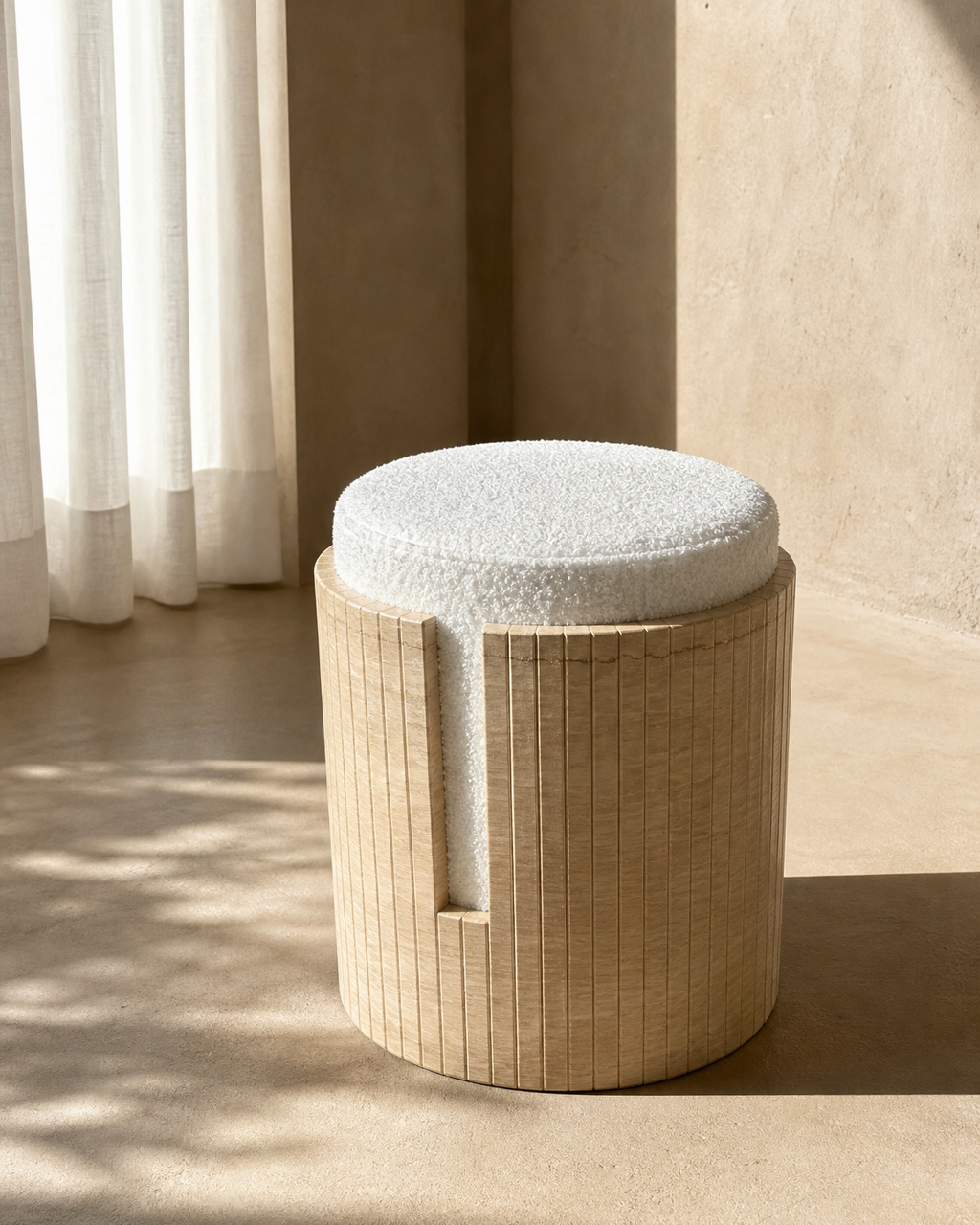 A cylindrical travertine stool with a round off-white textured cushion, set in a minimalist room with warm sunlight and neutral beige walls.