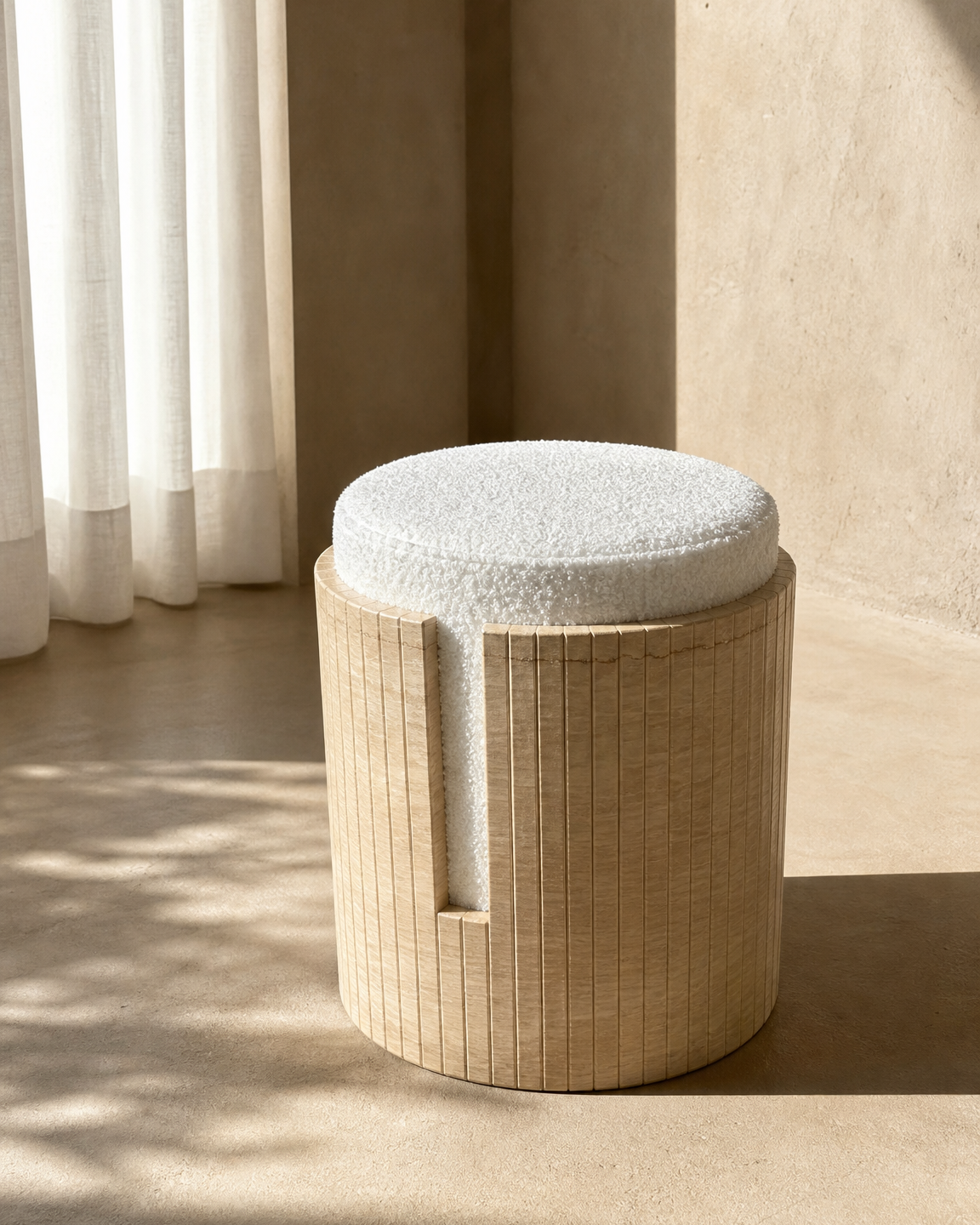 A cylindrical travertine stool with a round off-white textured cushion, set in a minimalist room with warm sunlight and neutral beige walls.
